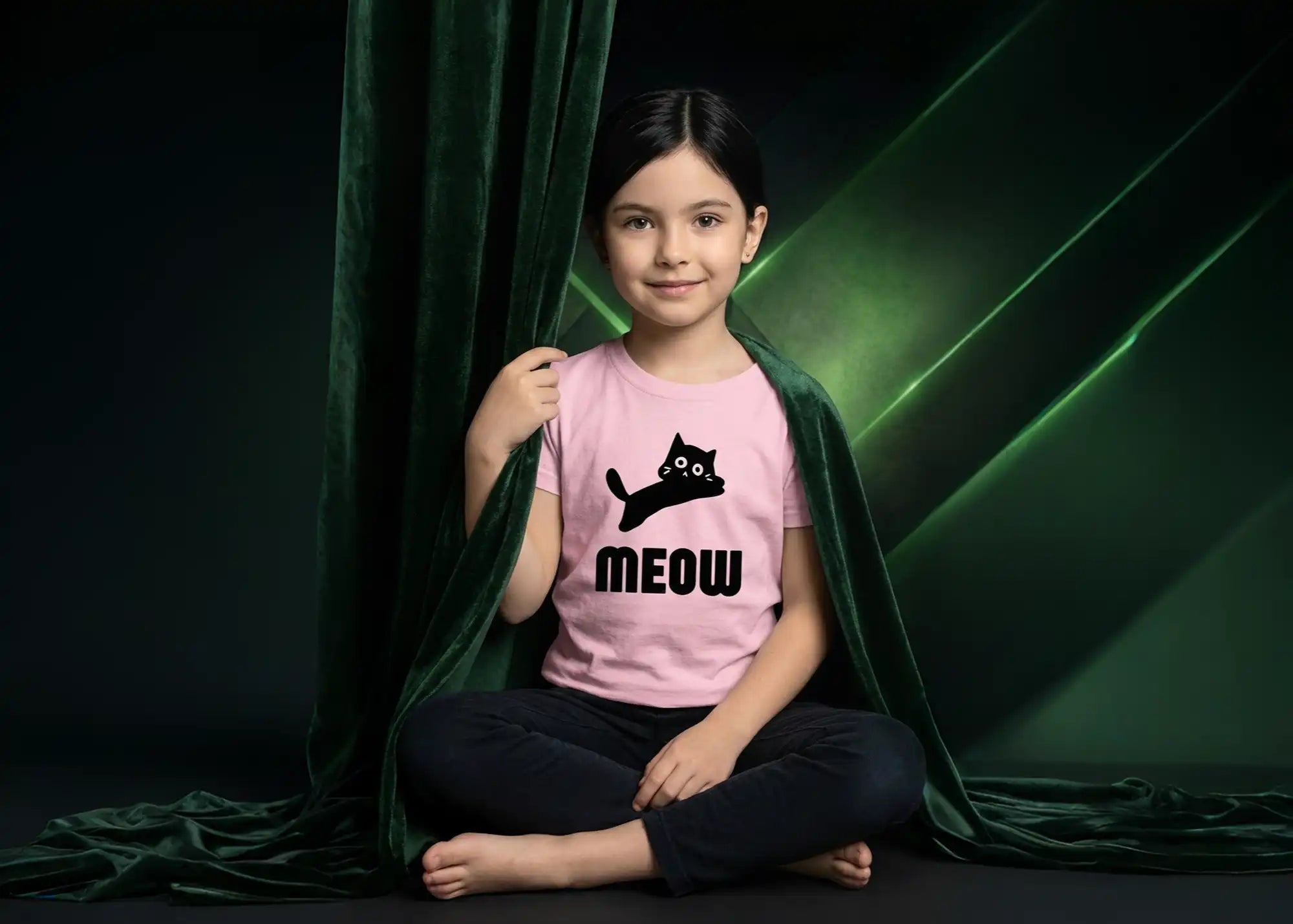 Child wearing a pink t-shirt with a cat graphic and 'MEOW' text, sitting against a dark green curtain.